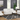 A living room featuring a white, ribbed fabric reclining sofa set, consisting of a three-seat sofa, loveseat, and an armchair. The furniture is placed on a geometric-patterned rug, with large windows offering natural light in the background. The decor includes a modern plant, table lamp, and artwork on the walls.
