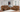 A cozy living room featuring a brown leather reclining sofa set including a reclining loveseat with cupholders, and a comfortable sofa. The furniture is arranged around a light-colored rug, with large windows providing natural light.